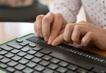 A blind woman uses a computer with a Braille display and a computer keyboard. Inclusive device