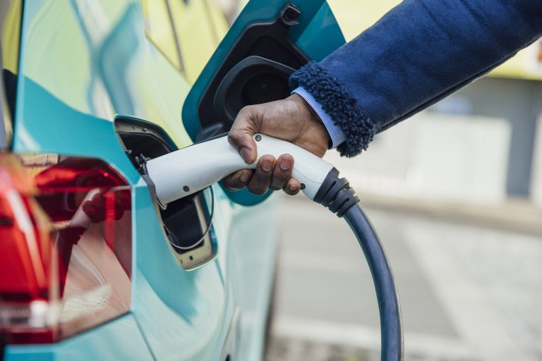 A side view close up shot of an unrecognisable mid adult businessman wearing formal businesswear putting his electric car on charge at a public charging point in Newcastle upon Tyne in the North East of England.