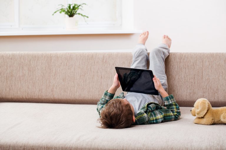 Cute little boy playing with a tablet pc on sofa at home