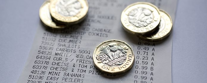 Five UK one pound coins placed on a till receipt.