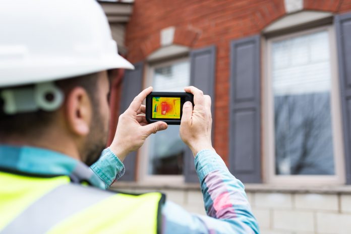 Engineer using thermal camera to analyse the heat loss of a house