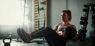 A beautiful and strong athletic young woman working hard cross fitness workout in low light gym working with medicine ball.