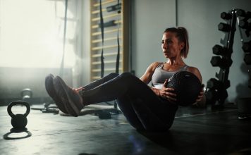 A beautiful and strong athletic young woman working hard cross fitness workout in low light gym working with medicine ball.