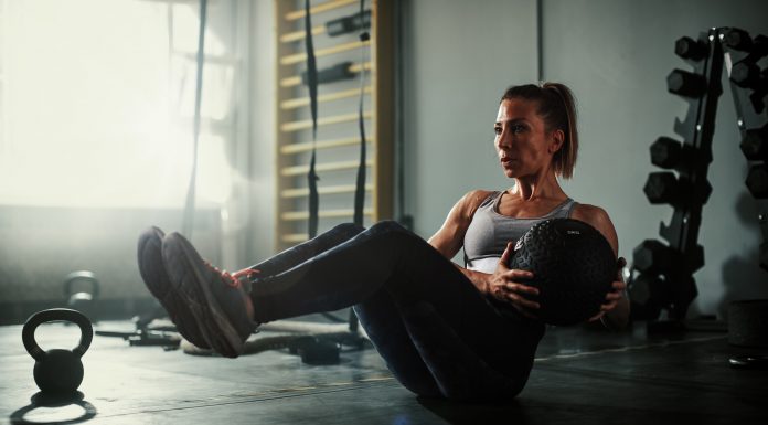 A beautiful and strong athletic young woman working hard cross fitness workout in low light gym working with medicine ball.