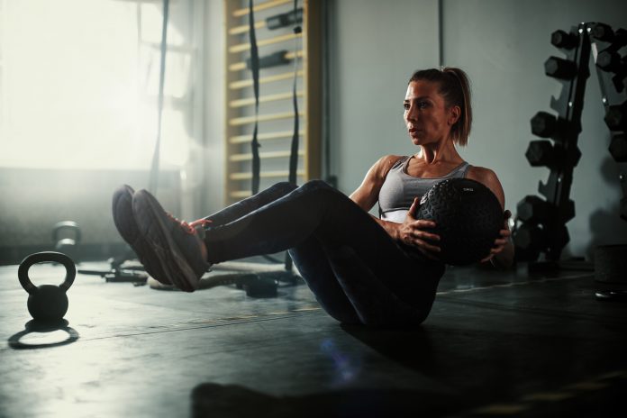 A beautiful and strong athletic young woman working hard cross fitness workout in low light gym working with medicine ball.