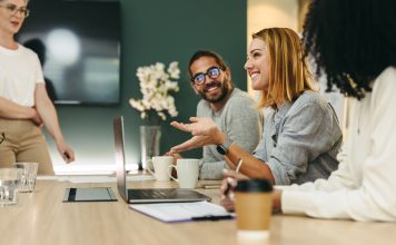 Business woman talking to her colleagues during a meeting in a boardroom. Group of happy business people working together in a creative office, social discourse and intellectual humility