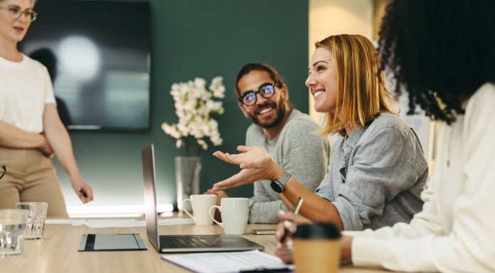 Business woman talking to her colleagues during a meeting in a boardroom. Group of happy business people working together in a creative office, social discourse and intellectual humility