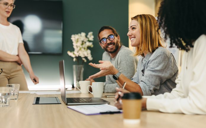 Business woman talking to her colleagues during a meeting in a boardroom. Group of happy business people working together in a creative office, social discourse and intellectual humility