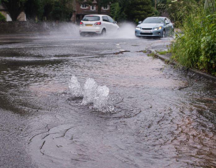 cars driving through flooded road caused by burst water main