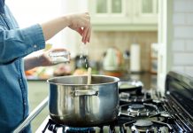 Woman adding salt to cooking pot on stove