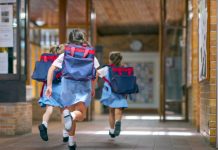 Rear view of excited students running towards entrance. Girls are carrying backpacks while leaving from school. Happy friends are wearing school uniforms, childhood education