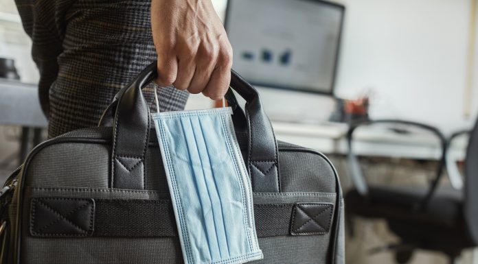 closeup of a young man in an office holding a briefcase and a surgical mask in his hand