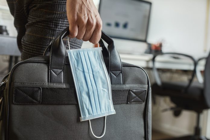 closeup of a young man in an office holding a briefcase and a surgical mask in his hand