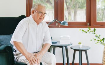 Old Asian senior man feel pain, ache, hurt at knee while standing and sitting at home, osteoarthritis concept