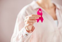 Close up of woman holding pink ribbon for breast cancer awarness. Detail of female hand holding pink awareness ribbon. Young woman supporting living with women's breast tumor.