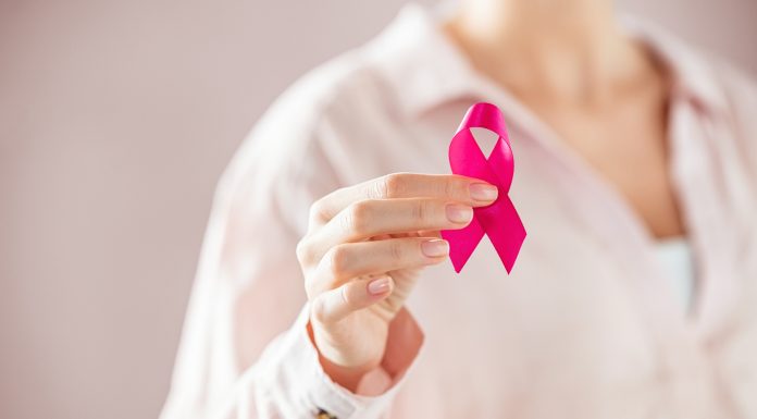 Close up of woman holding pink ribbon for breast cancer awarness. Detail of female hand holding pink awareness ribbon. Young woman supporting living with women's breast tumor.