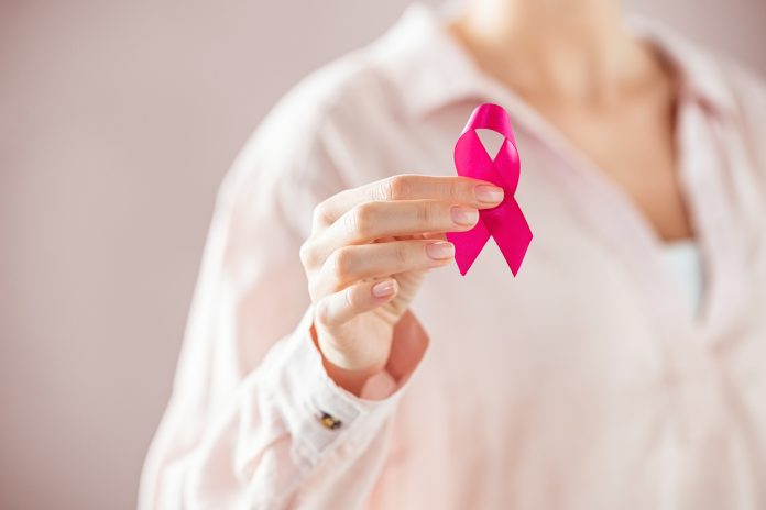 Close up of woman holding pink ribbon for breast cancer awarness. Detail of female hand holding pink awareness ribbon. Young woman supporting living with women's breast tumor.