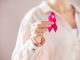 Close up of woman holding pink ribbon for breast cancer awarness. Detail of female hand holding pink awareness ribbon. Young woman supporting living with women's breast tumor.