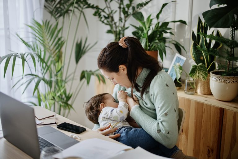 Mom is working on a computer, while breastfeeding her baby