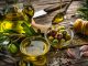 Close up view of two glass bowls filled with olives and extra virgin olive oil shot on rustic wooden table. A spoon pouring oil comes from the top right. Olive tree branches, garlic, salt and peppercorns complete the composition. High resolution 42Mp studio digital capture taken with Sony A7rII and Sony FE 90mm f2.8 macro G OSS lens