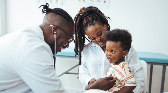 A happy toddler boy sits in his mother' lap at the pediatrician. He plays patacake with a doctor. Doctor giving prescription to african american mother with baby son at clinic. Medicine, healthcare and pediatry concept.