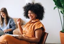 Black businesswoman smiling cheerfully while sitting in a meeting with her colleague. Happy young businesswomen working together in a modern workplace - female entrepreneurship