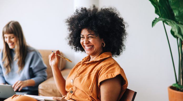 Black businesswoman smiling cheerfully while sitting in a meeting with her colleague. Happy young businesswomen working together in a modern workplace - female entrepreneurship