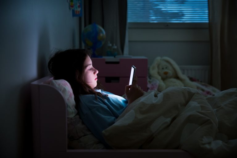 A child using smart phone lying in bed late at night, playing games, watching videos online, scrolling screen. Children's screen addiction. Child's room at night.