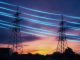 Electricity transmission towers with blue glowing wires against sunset sky background. Energy infrastructure concept.