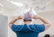 Female surgeon tying surgical mask in operation theater at hospital