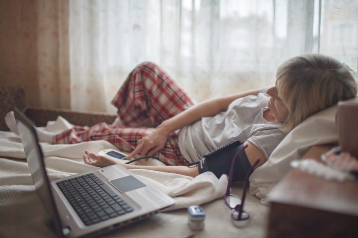 Old woman in bed looking at screen of laptop and consulting with a doctor online at home, telehealth