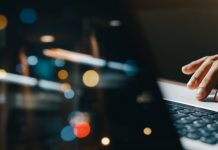 young man hand working on a laptop, bokeh blurred at night For text copy space, image size horizontal.