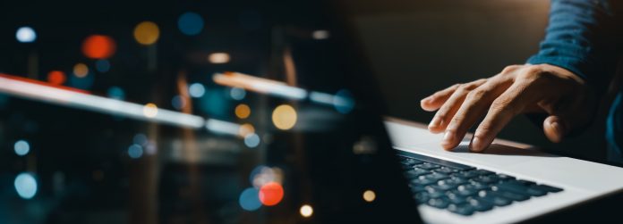 young man hand working on a laptop, bokeh blurred at night For text copy space, image size horizontal.