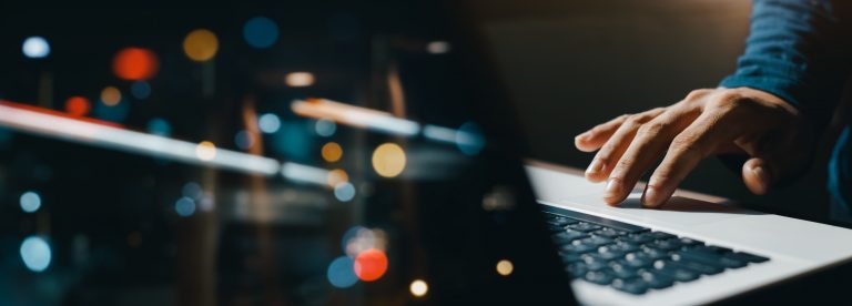 young man hand working on a laptop, bokeh blurred at night For text copy space, image size horizontal.