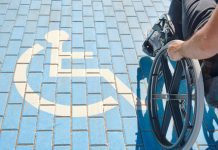 unrecognizable handicapped man in a wheelchair passing over blue and white handicapped sign painted on the floor, disability benefits CUT