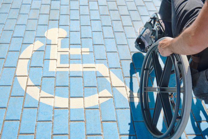 unrecognizable handicapped man in a wheelchair passing over blue and white handicapped sign painted on the floor, disability benefits CUT