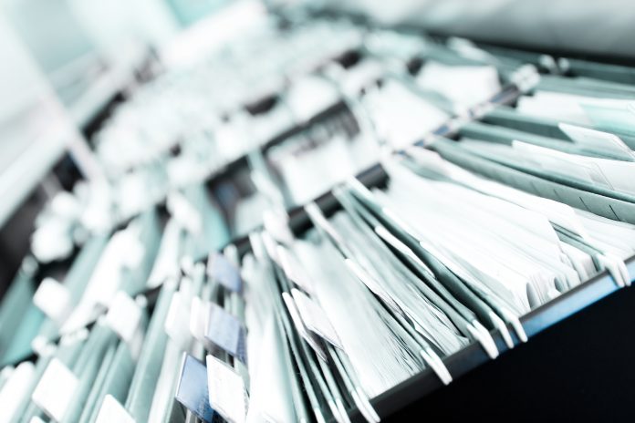 Multiple rows of filing cabinets in an office or medical establishment, overflowing with files. Narrow depth of field to emphasize the "neverending" feeling - tackling health and social care sectors and patient care
