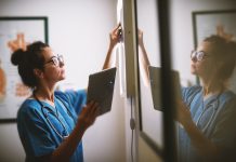 healthcare worker taking notes on white board with ipad in hand