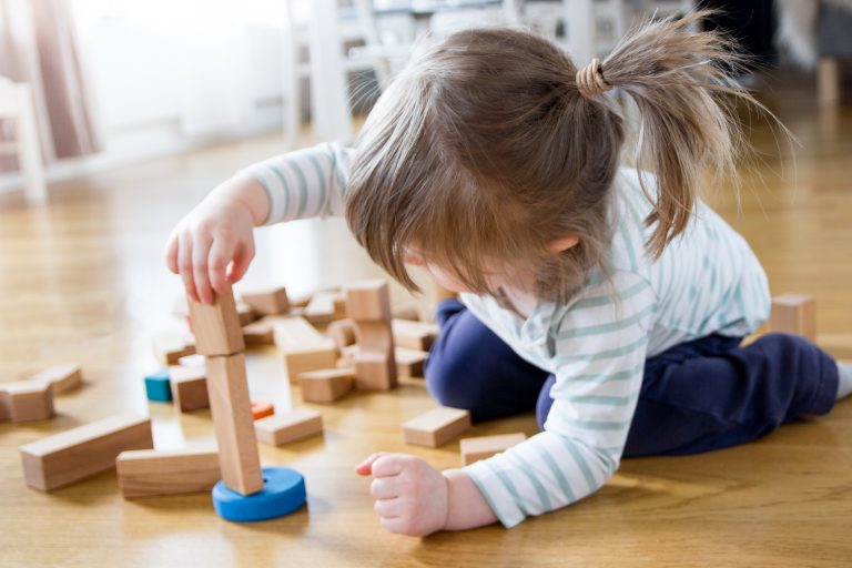 2 year old girl is playing and building a tower of wooden toy blocks