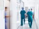 Motion Blur Shot Of Medical Staff Wearing Scrubs In Busy Hospital Corridor