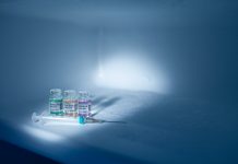 Compartment of refrigerator with set of bottles with COVID-19 (SARS-CoV-2) Coronavirus vaccine vials and injection syringe. Copy space provided.