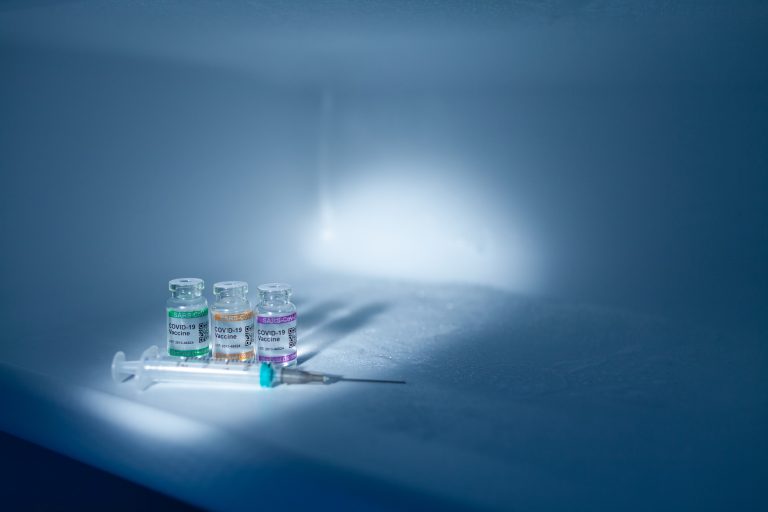 Compartment of refrigerator with set of bottles with COVID-19 (SARS-CoV-2) Coronavirus vaccine vials and injection syringe. Copy space provided.