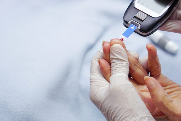 Doctor wear gloves is using lancet on a patient's finger.