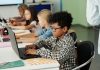 Side view of youthful African American schoolboy working in front of laptop