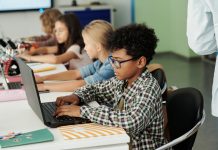 Side view of youthful African American schoolboy working in front of laptop