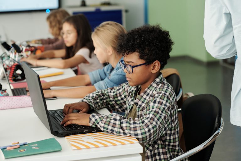 Side view of youthful African American schoolboy working in front of laptop