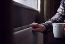 Close Up Of Mature Man Trying To Keep Warm By Radiator At Home During Cost Of Living Energy Crisis