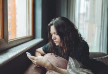 Depressed woman sitting on sofa at home with mobile