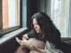 Depressed woman sitting on sofa at home with mobile