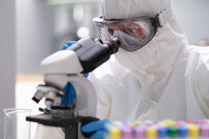 Scientist chemist in protective anti-plague suit looking through microscope in laboratory